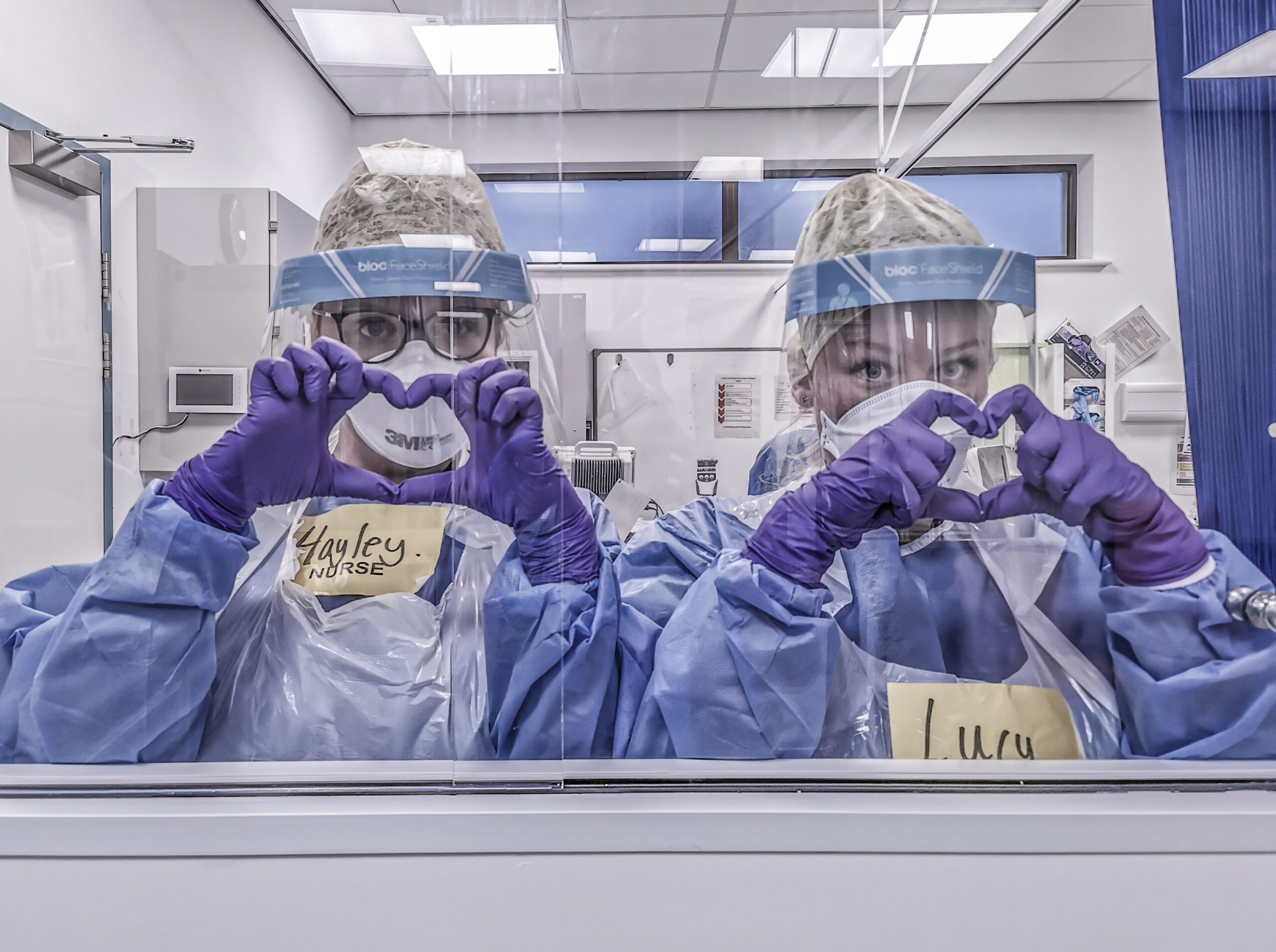 Two hospital workers in protective clothing making heart shapes with their hands